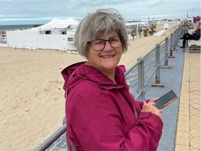 Vrouw die altijd zorgt. Ontspannen op vakantie in cyclaamkleurig jack leunend tegen de balustrade van de boulevard