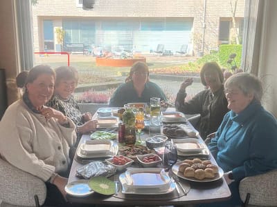 Vijf vrouwen zitten lachend en zelfverzekerd rond een gedekte tafel, zoals vrouwen die een reiki cursus volgden en na jaren nog steeds de werking ervan ervaren in hun dagelijks leven.