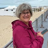 Vrouw die altijd zorgt. Ontspannen op vakantie in cyclaamkleurig jack leunend tegen de balustrade van de boulevard