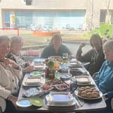 Vijf vrouwen zitten lachend en zelfverzekerd rond een gedekte tafel, zoals vrouwen die een reiki cursus volgden en na jaren nog steeds de werking ervan ervaren in hun dagelijks leven.